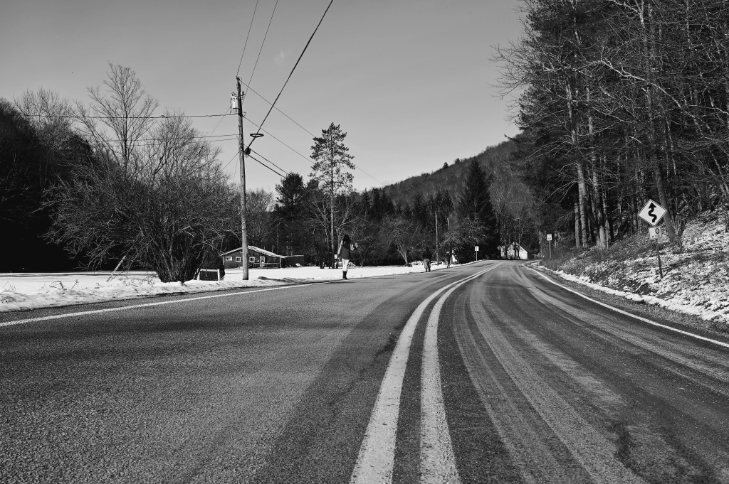 Black and white photograph of three pedestrians walking down a country road in the winter.